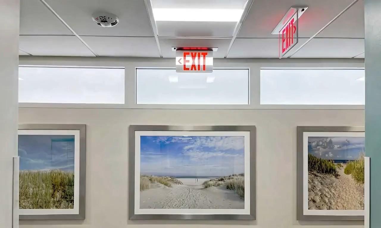 Innerscene Circadian Sky units placed above paintings on wall inside commercial building with an exist sign in front